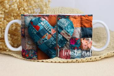 Weißer Keramikbecher mit einem Patchwork-Design in Form eines Herzens. Der Hintergrund besteht aus verschiedenfarbigen Stoffstücken in Blau-, Rot- und Orangetönen. Auf dem Becher steht in einer geschwungenen weißen Schrift: 'I love to craft'. Der Becher l